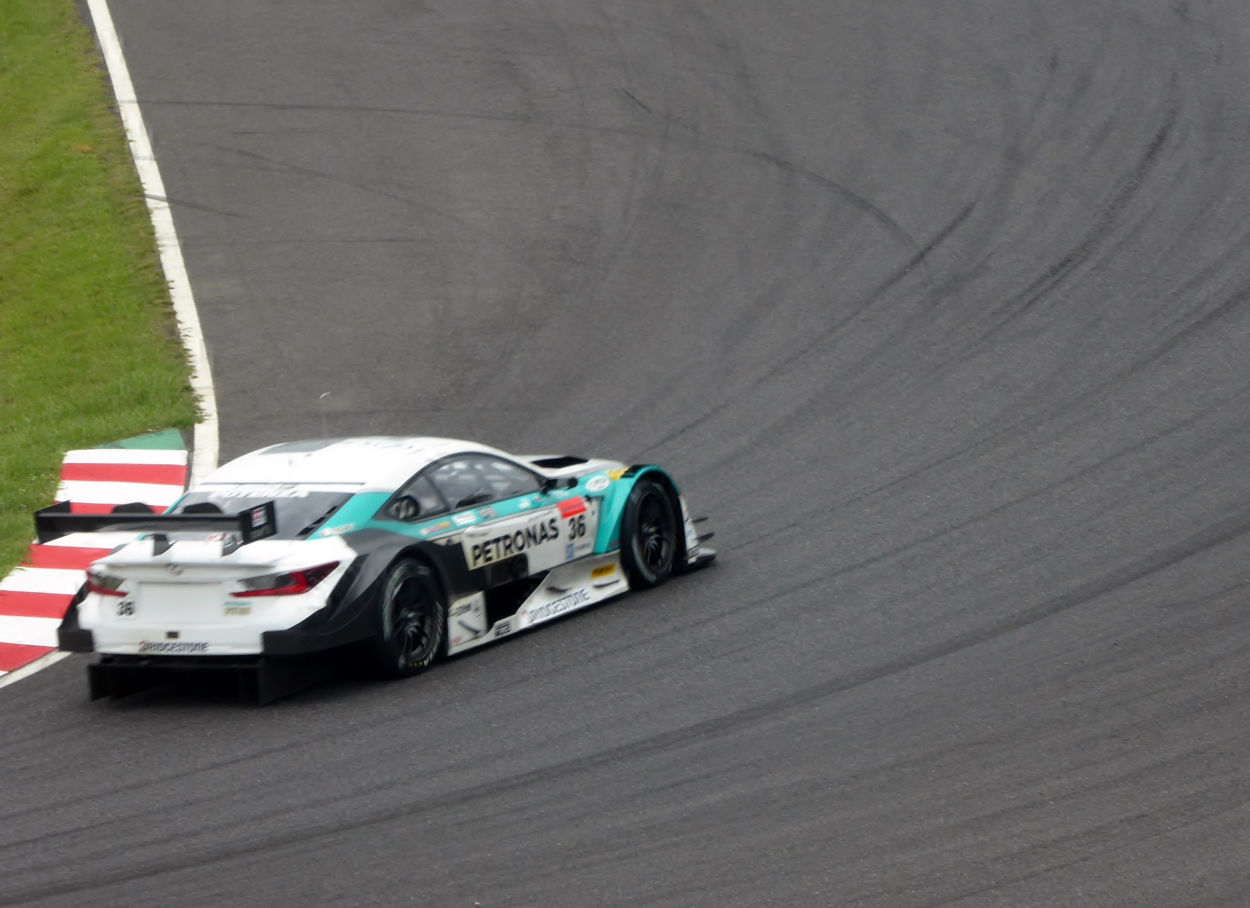 Ein silberner Mercedes-AMG GT3 Rennauto auf einer Rennstrecke mit Text auf der Karosserie und Gras links daneben.