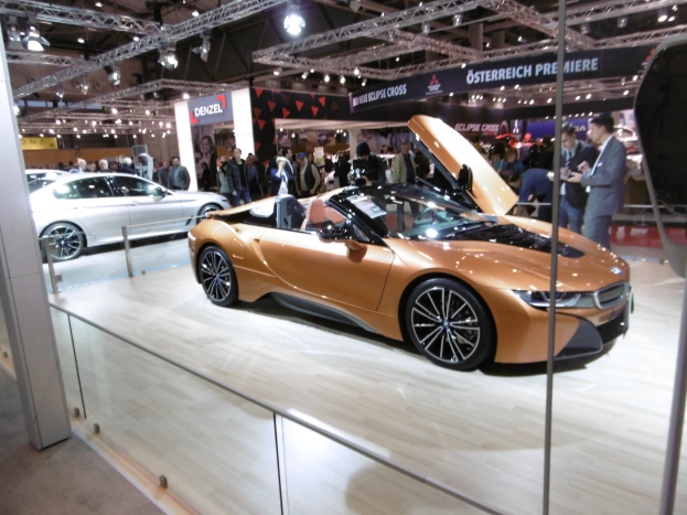 Ein schickes schwarzes BMW i8 Roadster mit Chromakzenten auf der Frankfurt Motor Show umgeben von formell gekleideten Gästen in einer Atmosphäre der Aufregung.
