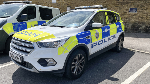 Zwei Polizeiautos nebeneinander auf einem Parkplatz geparkt, mit einer Wandmontage im Hintergrund.