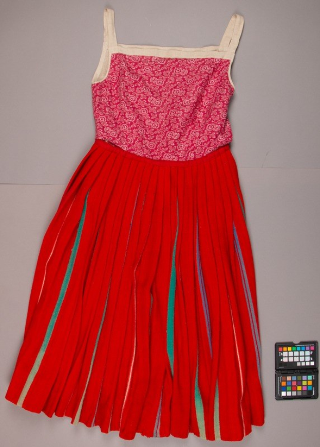 Ein rotes Kleid mit pinkem Oberteil und grünen Streifen liegt neben einem leuchtenden Farbpaletten.