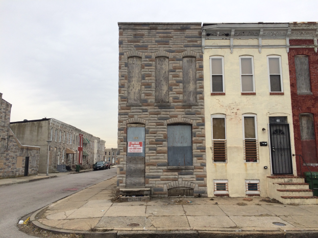 Ein altes, baufälliges Gebäude an einer Straßenecke mit zerbrochenen Fenstern, bröckelnden Wänden, vorbeifahrenden Fahrzeugen, Mülltonnen auf dem Gehweg und einem klaren blauen Himmel.