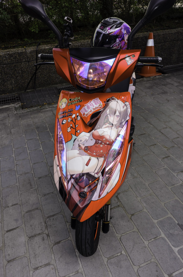 Ein oranger Roller mit Helm auf einer Straße geparkt, mit einem Verkehrskegel, einer Wand und Bäumen im Hintergrund.