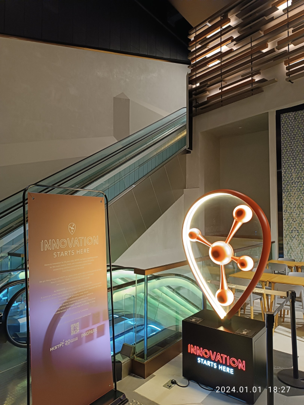 Großes Schild mit der Aufschrift "Innovation beginnt hier" in einem Gebäude mit einer Rolltreppe im Hintergrund, Tische und Stülhle auf der rechten Seite und ein Expo-Banner mit der Aufschrift "HSTP20 Expo" auf der linken Seite.