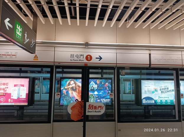Eine U-Bahn mit Glastüren und digitalen Bildschirmen an einem Bahnhof, mit Textanzeigen an der Wand und Deckenbeleuchtung.