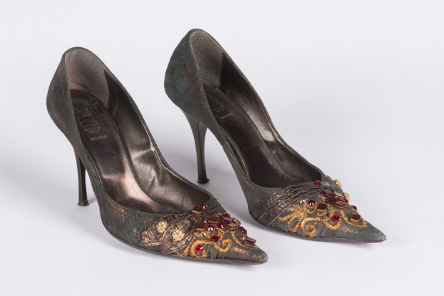 Ein Paar grüne High Heels mit goldenen und roten Kristallen, spitzer Zehe und Stiletto-Absatz, vor einem weißen Hintergrund.