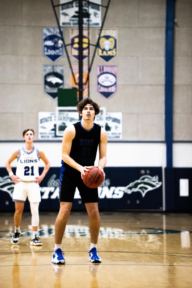 Ein Mann in Sportkleidung steht auf einem Basketballfeld und hält einen Basketball, mit Bannern im Hintergrund.