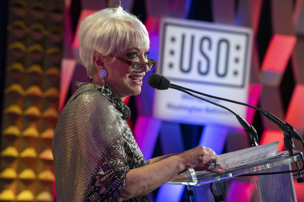 Frau an einem Rednerpult mit einer Brille und einem Blatt Papier, vor einem unscharfen Hintergrund, wahrscheinlich bei der Verleihung einer Auszeichnung für das Lebenswerk.