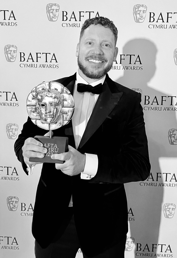 Ein Mann im Smoking, der eine BAFTA-Trophäe hält und lächelt, mit einem Hintergrundplakat mit der Aufschrift "BAFTA Awards 2018."