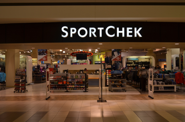 Ein Sportchek-Laden in einem Einkaufszentrum mit Kleiderstangen, Deckenleuchten, Säulen und einem Fernseher.