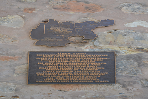 Metallplatte mit einer Deutschlandkarte und beschriftetem Text auf einem Steinmauer montiert.