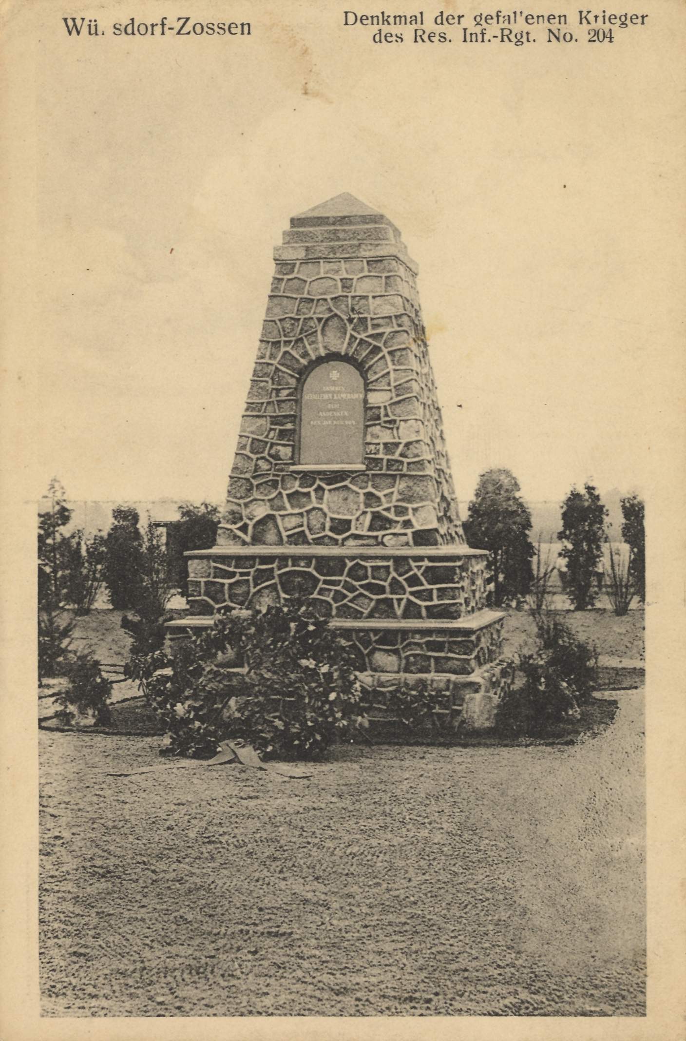 Steindenkmal mit der Aufschrift "Kriegsmarine-Mahnmal in Kriegsmann" in einem von Bäumen und Pflanzen umgebenen Park.