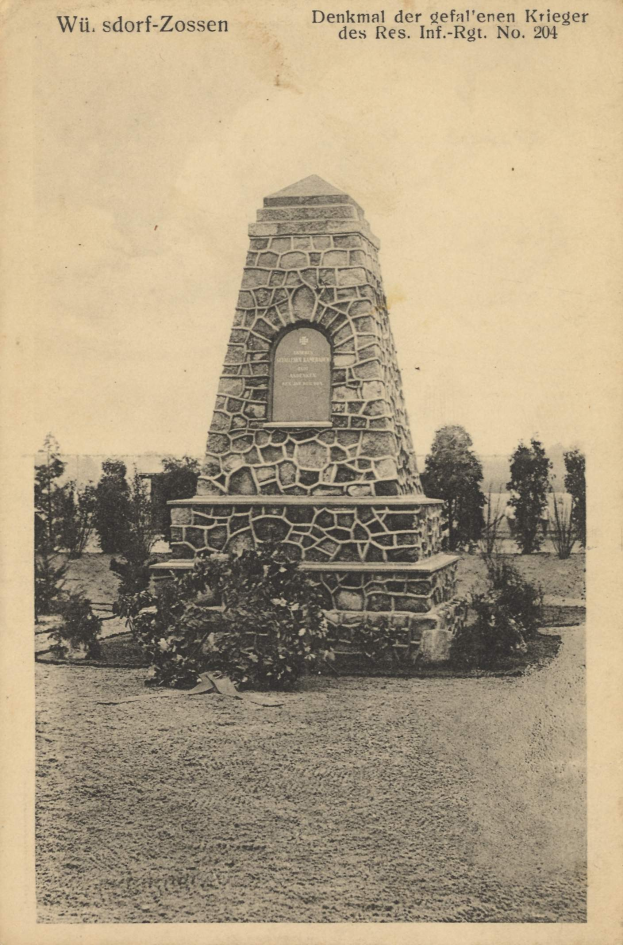 Steindenkmal mit der Aufschrift "Kriegsmarine-Mahnmal in Kriegsmann" in einem von Bäumen und Pflanzen umgebenen Park.