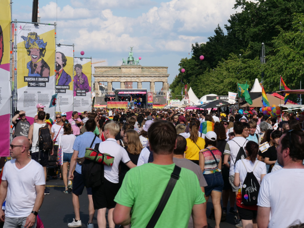 Große Menschenmenge marschiert am Brandenburger Tor in Berlin vorbei, mit Bannern, Zelten, Luftballons und einem Bogen im Hintergrund.