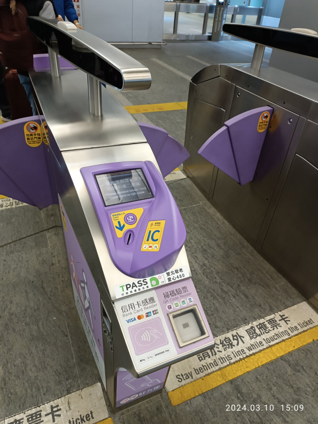 Gruppe von Menschen vor einem Metalldetektor an einem Bahnhof, mit einem weiteren Metalldetektor rechts und zusätzlichen Menschen im Hintergrund