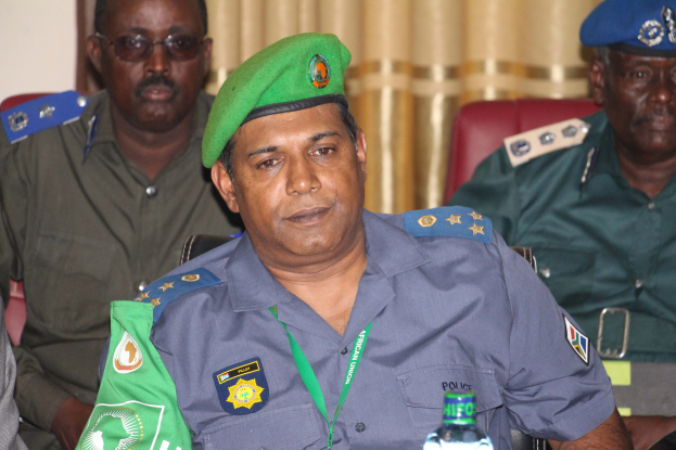 Gruppe von Männern an einem Tisch mit Wasserflaschen und Gegenständen, einer in Polizeiuniform, mit einem Vorhang und einer Wand im Hintergrund.