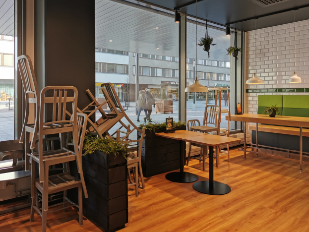 Innenansicht eines Berliner Restaurants mit Holztischen und -stühlen vor einem großen Fenster, das Fußgänger, Gebäude und Straßenelemente zeigt.