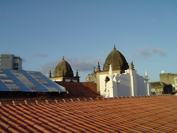 Stadtpanorama mit Gebäuden im Vordergrund und einem blauen Himmel im Hintergrund, das solarbetriebene Energie durch Solarpanele auf einem Dach anzeigt.