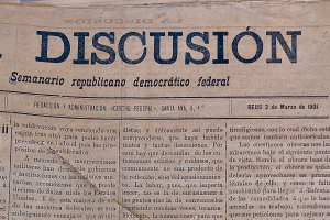 Eine gelbliche, leicht zerknitterte Zeitung mit der schwarzen Schrift 'Diskussion' darauf, die die Schlagzeile 'Semanario Republicano Democratico Federal' trägt.