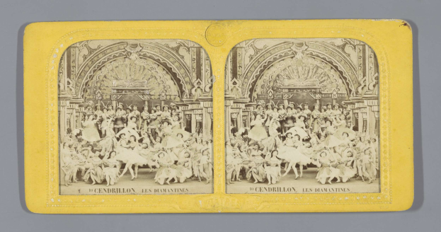 Schwarz-weiß-Foto von Menschen in bunten Kostümen, die vor einem Gebäude mit aufwändigen Verzierungen tanzen.