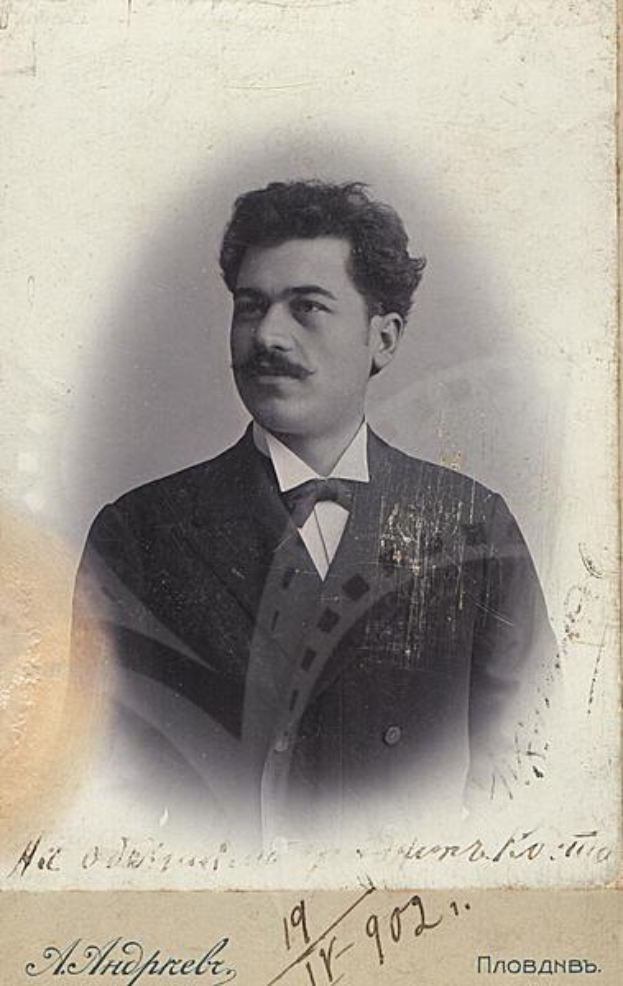 Ein altes Foto eines Mannes in Anzug und Krawatte mit Schnurrbart, der ernst dreinschaut, mit russischer Schrift unten.