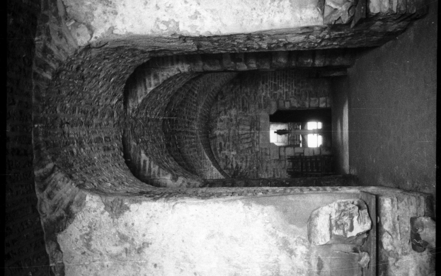 Schwarzes und weißes Foto eines Tunnels mit einem Fenster, das von einem Geländer umrahmt ist.