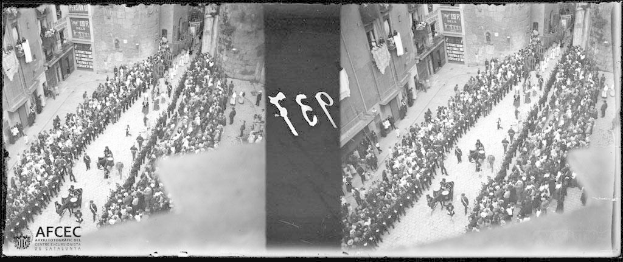 Ein Schwarz-Weiß-Foto einer großen Menge trauernder Menschen, die eine Straße entlanggehen, mit Gebäuden im Hintergrund.