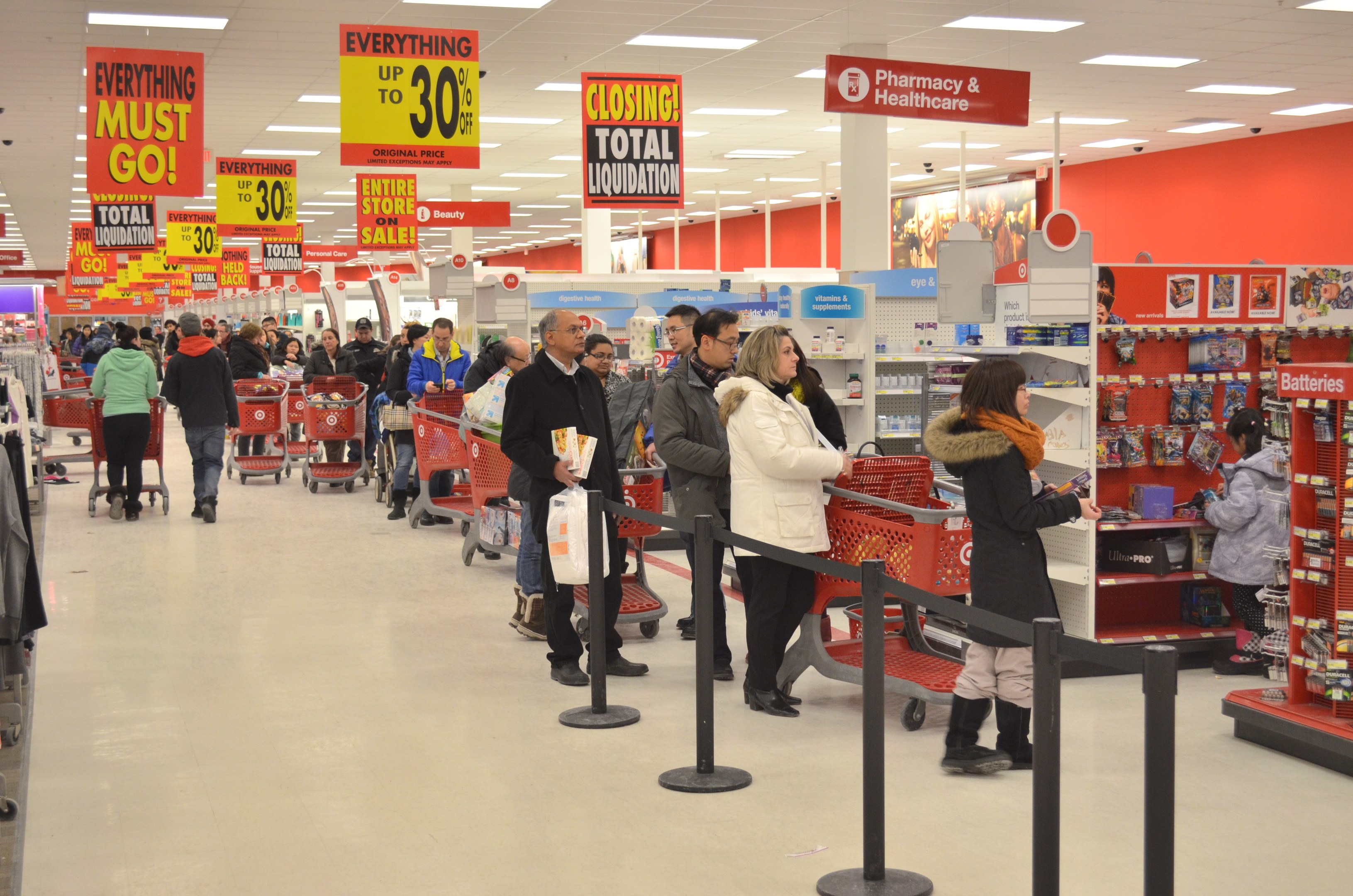 Ein volles Walmart-Geschäft während des Black Friday, mit Einkaufswagen schiebenden Kunden, Taschen haltenden Kunden und Waren durchsuchenden Kunden unter Deckenleuchten und nahe an Bändern befestigten Pfosten.