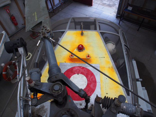 Nahaufnahme eines Hubschraubers auf einem Gebäudeboden, mit einem Feuerlöscher links daneben und einer Bank rechts daneben, was Wartungsaktivitäten anzeigt.