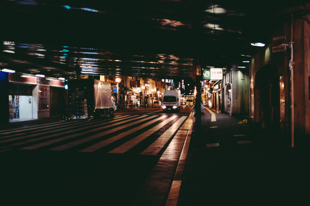 Stadtstraße bei Nacht mit Fahrzeugen, Gebäuden auf beiden Seiten, beleuchtet von Lichtern und eine Brücke im Hintergrund.
