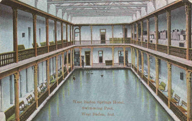 Schwarz-weiß-Postkarte des großen Innenpools des West Baden Springs Hotels mit Menschen, Säulen, Geländern, Stühlen und Text am unteren Rand.