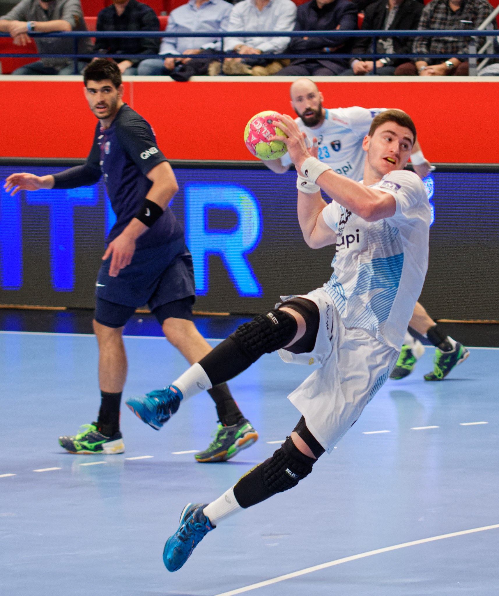 Eine Gruppe von Männern, die auf einem Feld während des Futsal-Weltmeisterschafts 2019 Handball spielen, mit Zuschauern im Hintergrund und einer Anzeigetafel mit Veranstaltungstagen.
