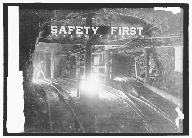 Schwarzes und weißes Foto eines Zuges, der durch einen Tunnel fährt, mit einer Person, die auf dem Gleis steht, und einem Schild mit der Aufschrift "Sicherheit geht vor."