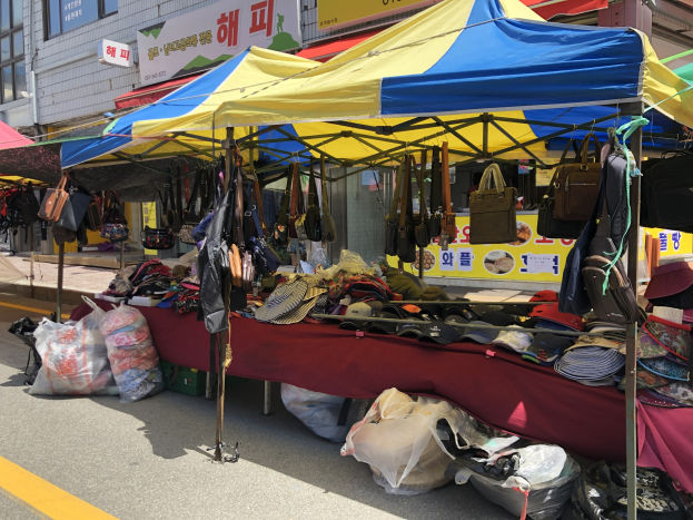 Ein Straßenmarkt mit Zelten, die Taschen, Hüte und andere Gegenstände ausstellen, vor einem Hintergrund von Gebäuden mit Fenstern und Texttafeln.