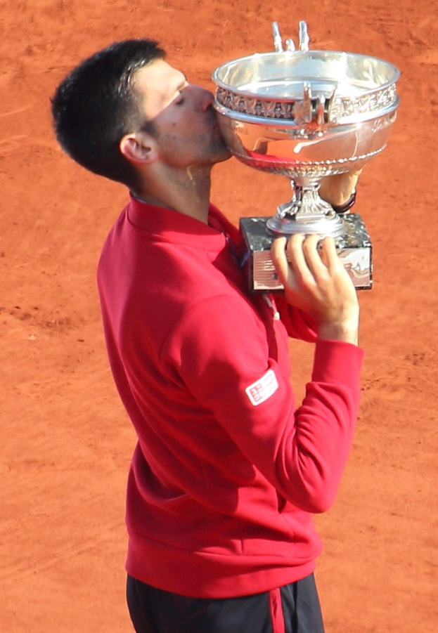 Novak Djokovic hält den French-Open-Pokal nach seinem Sieg gegen Rafael Nadal im Finale der Herren-Einzel, steht mit einem triumphierenden Gesichtsausdruck da und küsst den Pokal.