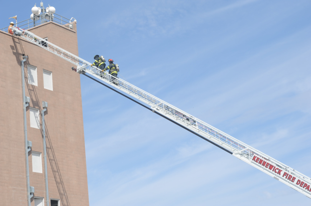 Feuerwehrleute in Schutzausrüstung arbeiten von einer Leiter aus, um ein Gebäude Feuer zu löschen, mit sichtbarem Mast und Fenstern an der Struktur.