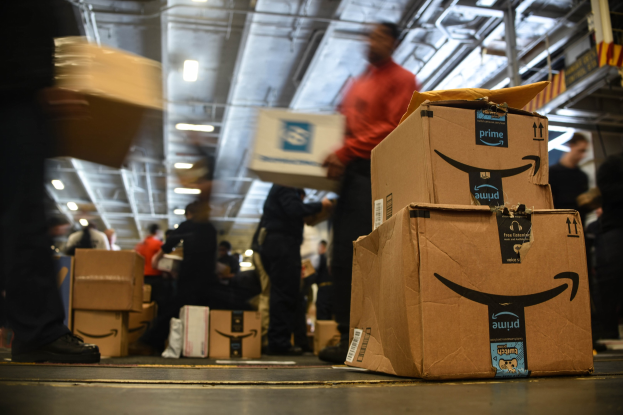 Mitarbeiter in einem Amazon-Versandzentrum, die Kartons stapeln und organisieren, unter Lagerbeleuchtung.