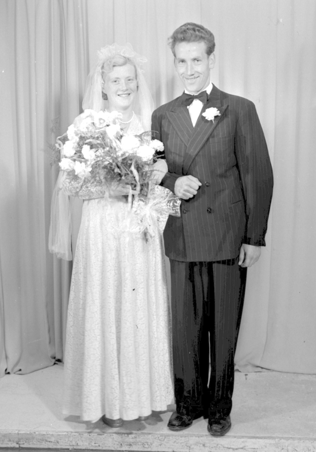 Ein Mann und eine Frau stehen Seite an Seite auf einer Bühne, lächeln und die Frau hält einen Blumenstrauß, und ein Vorhang hinter ihnen.