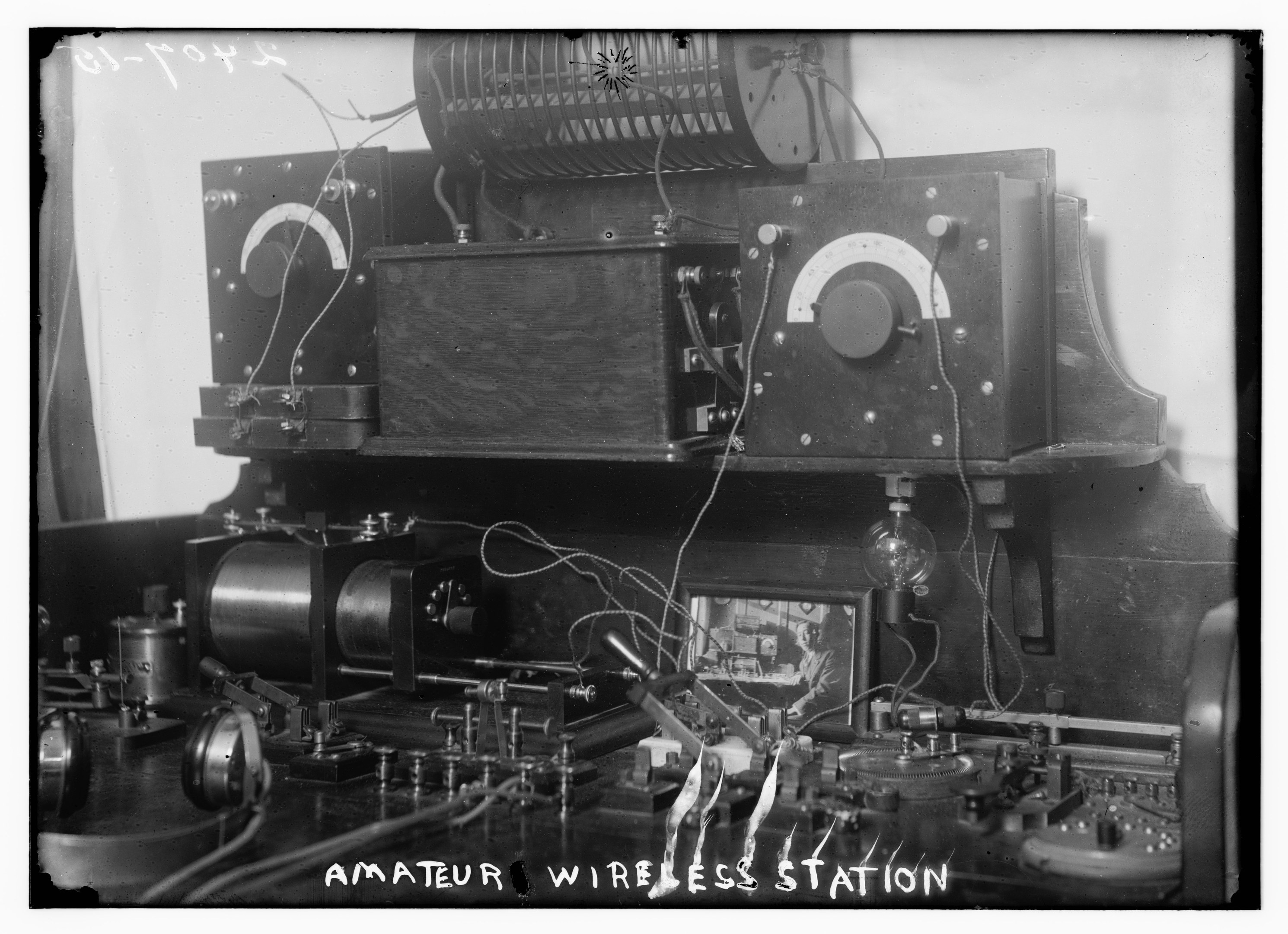 Schwarz-weiß-Foto einer Amateur-Funkstation mit elektronischen Geräten und Drähten, mit Text unten.