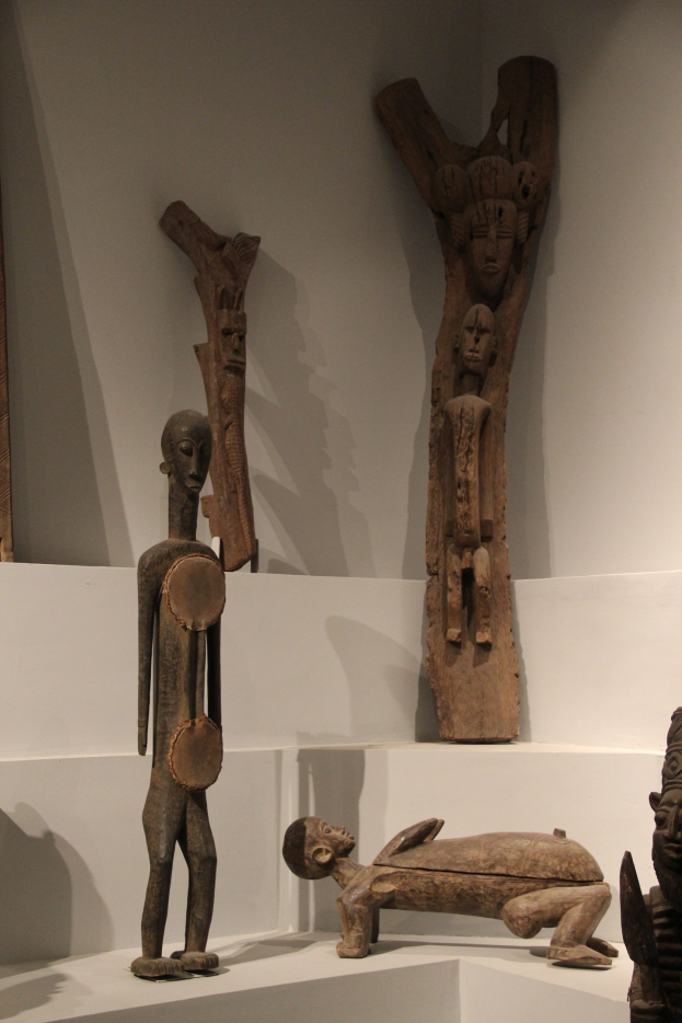 Gruppe von Holzskulpturen auf einer weißen Oberfläche in einem Museum ausgestellt, mit einer Wand im Hintergrund.