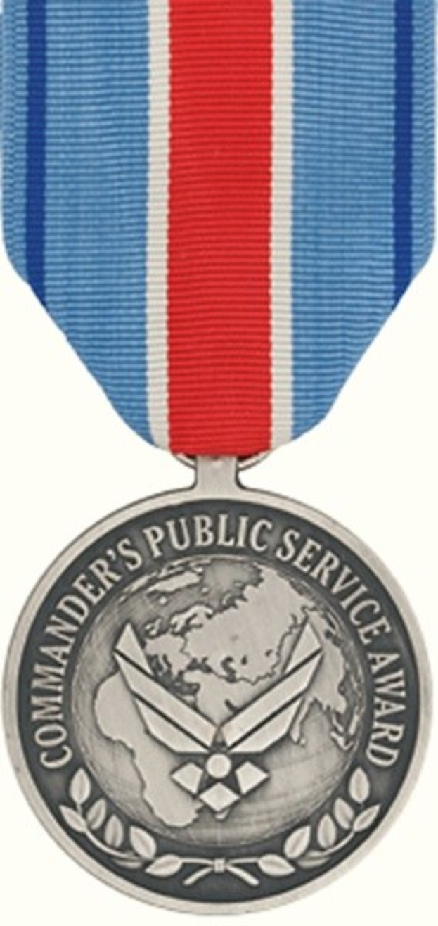 Silberne Medaille mit rot-weiß-blauem Band, beschriftet mit 'Commander's Public Service Award' vor weißem Hintergrund.