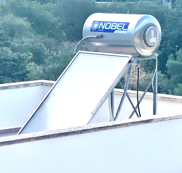 Solarwassererwärmer mit Speicher auf dem Dach eines Gebäudes, Bäume im Hintergrund.