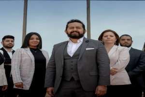 Eine Gruppe von Menschen, die vor einem Gebäude mit einer Glaswand und Himmel im Hintergrund stehen, identifiziert als Besetzung von 'The Real Housewives of Beverly Hills'.