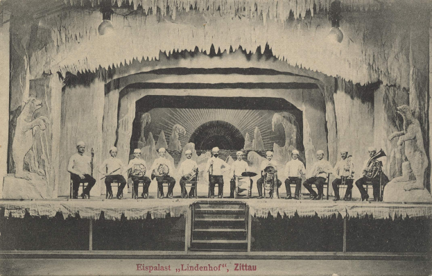 Schwarz-weiß-Foto einer Gruppe von Menschen auf einer Bühne mit Musikinstrumenten, mit Treppen, die hinaufführen, und Skulpturen auf beiden Seiten, beschriftet mit "Lindenhof, Zittau, Deutschland".