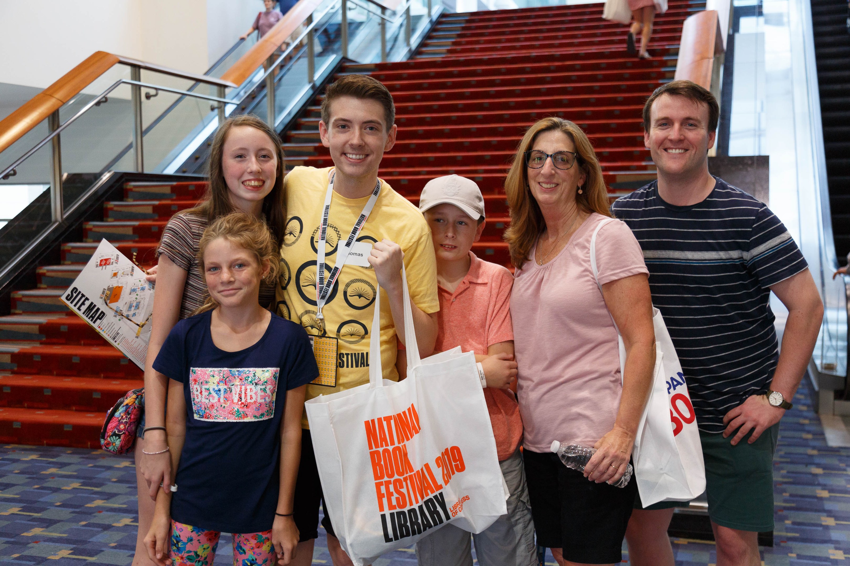 Gruppe von Menschen, die vor einer Rolltreppe an der Nationalen Buchmesse 2019 lächeln und Taschen halten