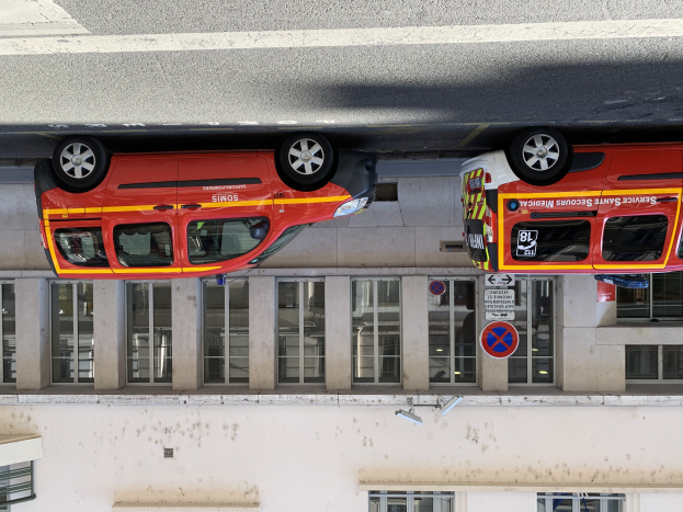 Zwei Krankenwagen nebeneinander in einer Garage geparkt mit einem Gebäude mit Glasfenstern und Schildern im Hintergrund und einer Überwachungskamera an der Wand unten im Bild.