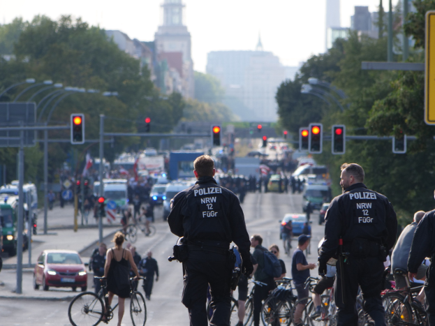 Polizeibeamte auf Fahrrädern eine von Bäumen gesäumte Straße mit Gebäuden und einem klaren blauen Himmel im Hintergrund.