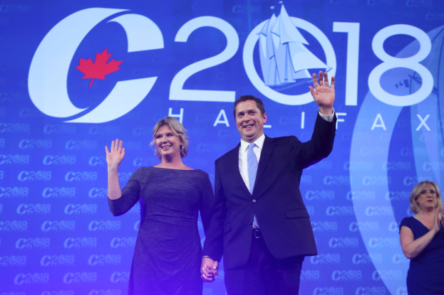 Ein Mann in einem schwarzen Blazer, weißem Hemd und blauer Krawatte sowie eine Frau, die klatscht, beide strahlend, stehen auf einer Bühne vor einem blauen Hintergrund mit einem "C2C 2018"-Schild.