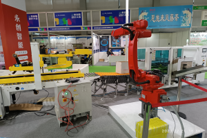 Eine Gruppe von Robotern auf einem Tisch in einer Fabrikumgebung, umgeben von Maschinen, Kabeln und anderer Ausrüstung, mit ein paar Menschen im Hintergrund.