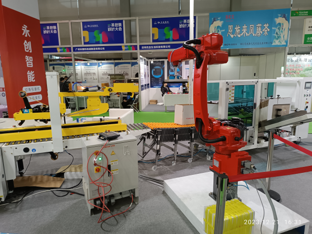 Eine Gruppe von Robotern auf einem Tisch in einer Fabrikumgebung, umgeben von Maschinen, Kabeln und anderer Ausrüstung, mit ein paar Menschen im Hintergrund.