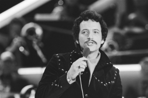 Schwarzes und weißes Foto von Elvis Presley, der ein Mikrofon während einer Live-Aufführung hält, mit einem unscharfen Hintergrund.